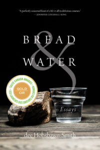 A chunk of bread sitting on a wooden table next to a glass of water. The background is black.